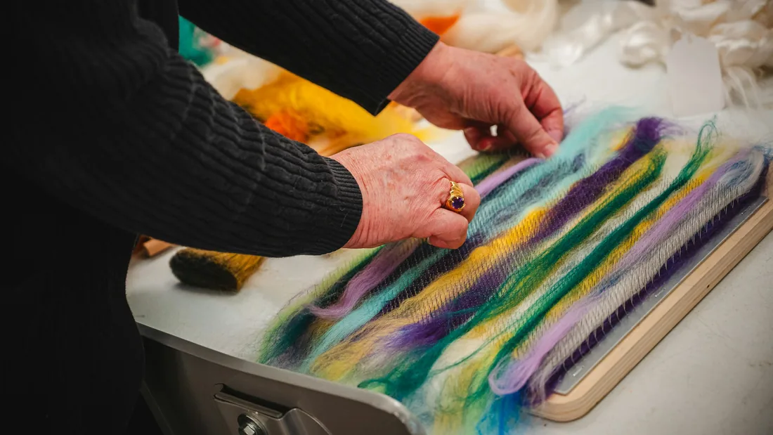 Manos colocando mechas de lana de colores sobre una mesa de trabajo de fieltro
